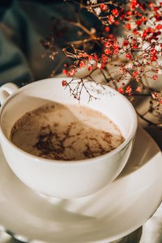 White cup of milk and chocolate. Morning aesthetics vibes. Breakfast. Pink gypsophila flowers. Hard shadows.