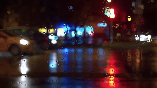 Rain water drops on window glass. Blurred night city traffic lights. City background