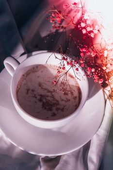 White cup of milk and chocolate. Morning aesthetics vibes. Breakfast. Pink gypsophila flowers. Hard shadows.