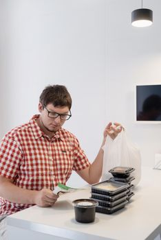 Delivery food, products to home. Shopping and healthy food concept. Young man in red plaid shirt Young man sorting food delivery boxes at the modern kitchen at the modern kitchen