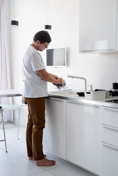 Doing chores. Man in white shirt washing dishes in the modern kitchen. Minimal modern kitchen interior