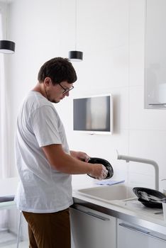 Doing chores. Man in white shirt washing dishes in the modern kitchen. Minimal modern kitchen interior