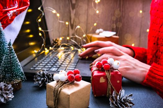 Christmas online shopping, work and education. New Year decorations on table. Woman with notebook computer at home. Winter holidays sales. Gift boxes, christmas trees. Garland light