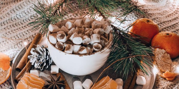 Cup with hot winter cacao and marshmallows tangerines spruce branch on bed. Christmas lights. Pine cones decoration. Cozy winter days. Hygge