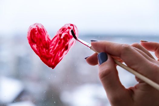 Hand of a girl with a paintbrush painting red heart on a window, stay home, quarantine leisure, let's all be well, Valentines day, Love, Romance