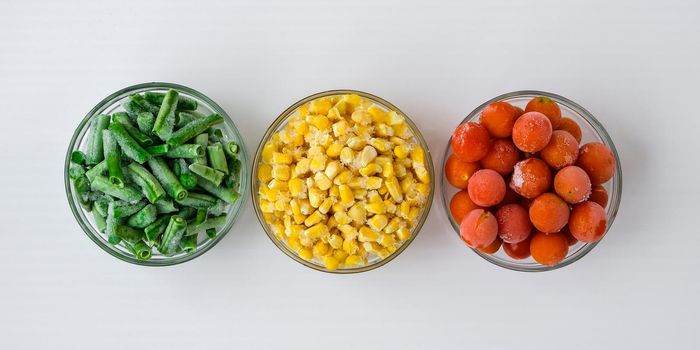 Three Bowls of frozen vegetables food of yellow corn, green beans, red tomatoes. Colors of traffic light. Harvest Food preservation for winter. Copy space