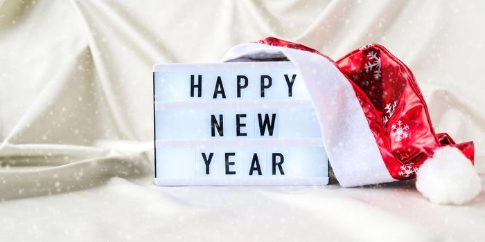 Lightbox with text HAPPY NEW YEAR with santa hat on silk fabric background. Winter holiday concept. Christmas and New Year