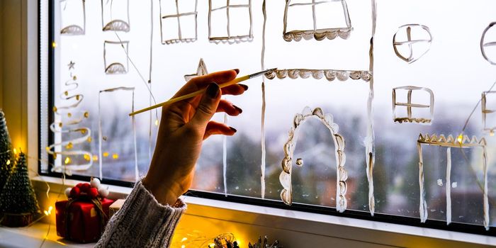 Female hand draws christmas holidays decoration painted on window glass. New Years scenery. city buildings garlands lights. hygge, decoration and christmas concept. festive garland string at home