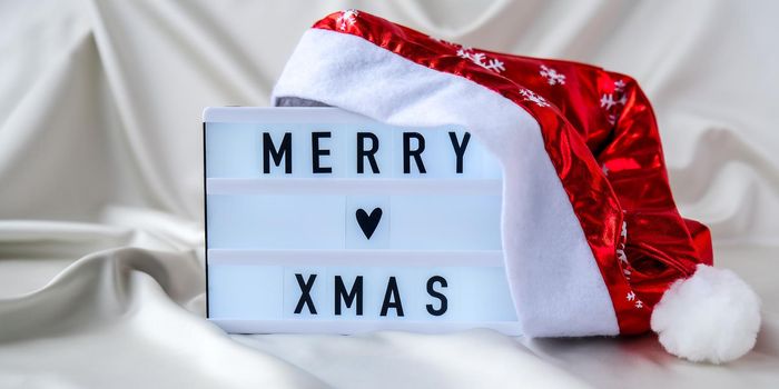 Lightbox with text MERRY XMAS with santa hat on silk fabric background. Winter holiday concept. Christmas and New Year