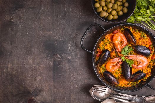 Paella background, space for text. Paella in black pan with saffron rice, peas, shrimps, mussels, squid, meat. Seafood paella, traditional spanish dish. Paella on rustic black wooden table. Top view