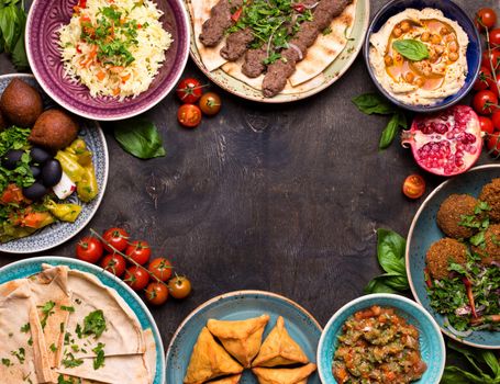 Middle eastern or arabic dishes and assorted meze on a dark background. Meat kebab, falafel, baba ghanoush, hummus, rice with vegetables, sambusak, kibbeh, pita. Halal food. Space for text. Top view