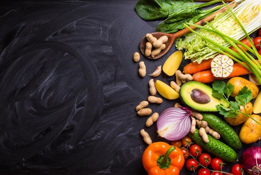 Vegetables, herbs, nuts, ingredients for cooking, wooden spoon on rustic black chalk board background. Healthy, clean eating concept. Vegan or gluten free diet. Space for text. Top view. Salad making