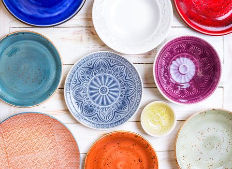 Different antique vintage multicolored empty plates and bowls on a white old wooden table. Table setting. Shabby chic/retro style. Top view. Tableware. Rustic kitchen. Set of plates