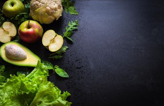 Fresh green vegetables and fruits on black chalk board background. Сauliflower, avocado, spinach, lettuce salad, green apples, herbs. Vegetarian food. Diet/healthy/detox food concept. Space for text