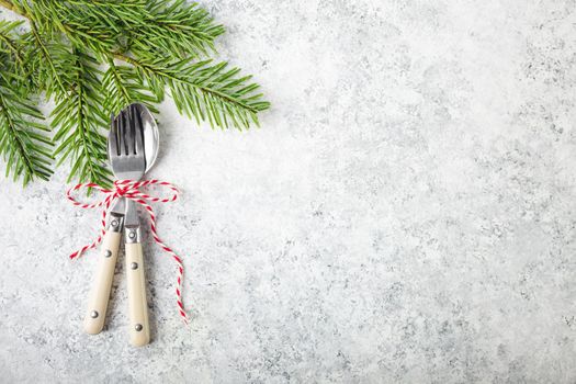 Christmas/New Year background. Christmas table place setting. Festive dinner background. Spoon, fork, fir branch on white concrete background. Christmas decoration. Space for text. Top view. Holidays