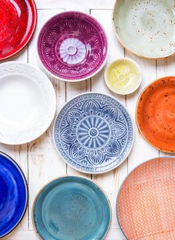 Different antique vintage multicolored empty plates and bowls on a white old wooden table. Table setting. Shabby chic/retro style. Top view. Tableware. Rustic kitchen. Set of plates