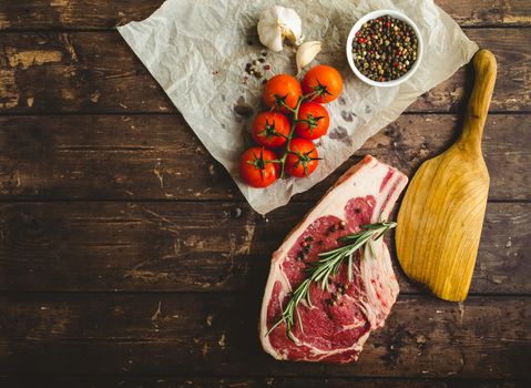 Raw marbled meat steak, pepper, herbs, tomato, old wooden background. Space for text. Beef Rib eye steak ready for cooking. Top view. Copy space. Ingredients, meat roasting. Ribeye meat steak. Closeup