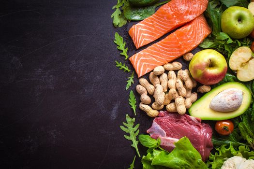 Fresh vegetables, fruits, fish, meat, nuts on black chalk board background. Сauliflower, avocado, apples, tomatoes, salmon, beef, spinach, herbs. Diet/healthy/paleo food. Ingredients. Space for text