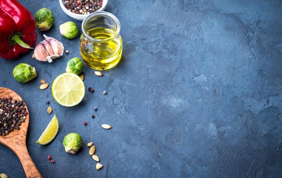 Ingredients for cooking. Olive oil in glass jar, wooden cooking spoon, spices, red bell pepper, lime, brussels sprout, garlic, colourful seasonings. Cooking ingredients background. Space for text