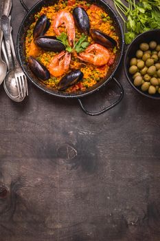 Paella background, space for text. Paella in black pan with saffron rice, peas, shrimps, mussels, squid, meat. Seafood paella, traditional spanish dish. Paella on rustic black wooden table. Top view