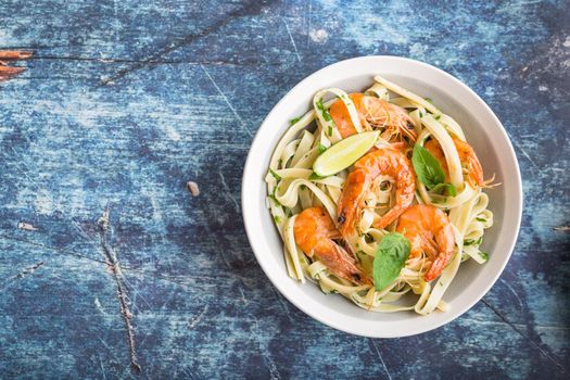 Homemade pasta with fried shrimps and basil on rustic wooden blue background. Space for text. Pasta with seafood in plate. Top view. Closeup. Mediterranean cuisine. Pasta for dinner or lunch. Overhead