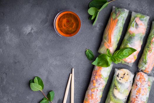 Fresh assorted spring rolls set background. Handmade asian/Chinese spring rolls, sauce, chopsticks. Rustic concrete background. Spring rolls with shrimps, vegetables, fruits. Space for text. Top view