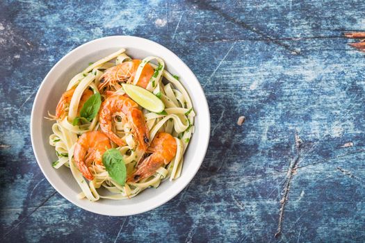 Homemade pasta with fried shrimps and basil on rustic wooden blue background. Space for text. Pasta with seafood in plate. Top view. Closeup. Mediterranean cuisine. Pasta for dinner or lunch. Overhead