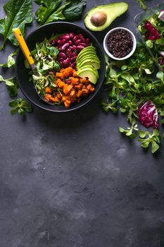 Quinoa salad in bowl with avocado, sweet potato, beans, herbs, spinat on concrete rustic background. Quinoa superfood concept. Clean healthy detox eating. Vegan/vegetarian food. Making healthy salad