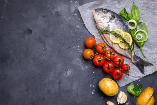 Raw fish with fresh ingredients ready to cook. Fish, lemon, herbs, potato, tomatoes. Ingredients for cooking on dark rustic background. Space for text. Diet and healthy food. Fish background. Top view