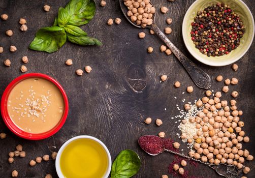 Hummus ingredients. Chickpea, tahini, olive oil, sesame seeds, sumac, herbs on dark rustic wooden background. Space for text. Set of ingredients for making hummus. Middle eastern cuisine. Top view