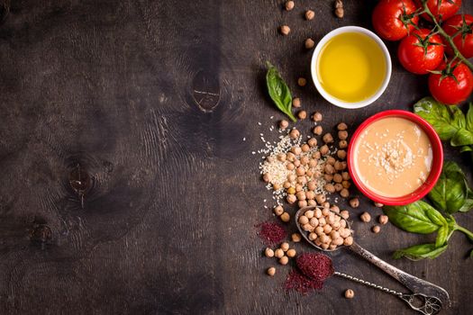 Hummus ingredients. Chickpea, tahini, olive oil, sesame seeds, sumac, herbs on dark rustic wooden background. Space for text. Set of ingredients for making hummus. Middle eastern cuisine. Top view