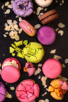 Assorted colorful french macarons and almond flakes on a black background. Closeup. Top view. Concept of the baking macarons