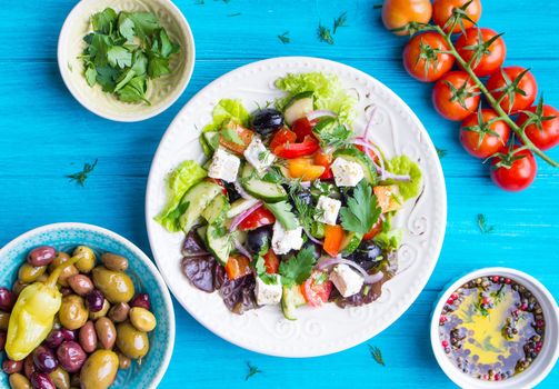 Greek salad bowl. Close-up. Bowl with fresh greek salad, tomatoes, olives, olive oil on wooden table. Healthy eating concept. Top view. Traditional greek dish. Making salad ingredients. Mediterranean