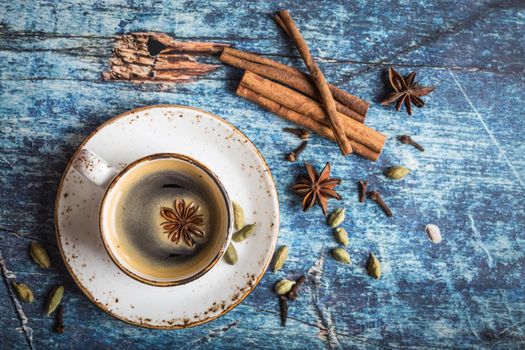 Cup of fresh hot coffee with spices on old rustic blue wooden table. Vintage background. Autumn/winter warming coffee. Black coffee, cinnamon. Espresso, white cup. Top view. Close up. From above