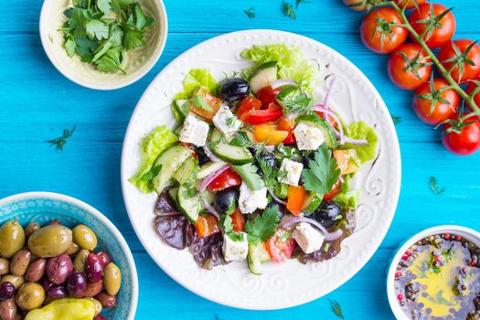 Greek salad bowl. Close-up. Bowl with fresh greek salad, tomatoes, olives, olive oil on wooden table. Healthy eating concept. Top view. Traditional greek dish. Making salad ingredients. Mediterranean