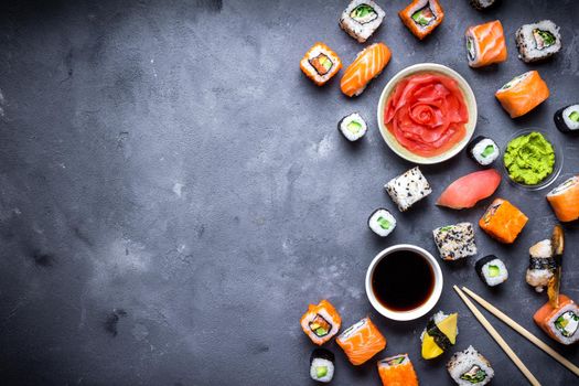 Japanese sushi on a rustic dark background. Sushi rolls, nigiri, maki, pickled ginger, wasabi, soy sauce. Sushi set on a table. Space for text. Top view. Sushi background. Asian or Japanese food frame