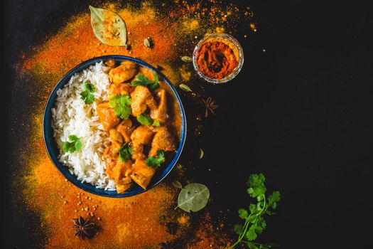 Indian Butter chicken with basmati rice in bowl, spices, black background. Space for text. Butter chicken, traditional Indian dish. Top view. Chicken tikka masala. Indian cuisine concept. Overhead