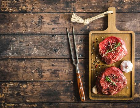 Raw marbled meat steak Filet Mignon with seasonings, fork, wooden cutting board. Space for text. Beef steak ready for cooking. Top view. Ingredients. Uncooked meat steak. Close-up. Rustic background