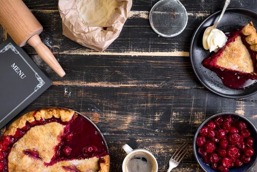 Baking background with sliced cherry pie, flour, rolling pin on the black wooden table. Ingredients for baking/dessert or pie making