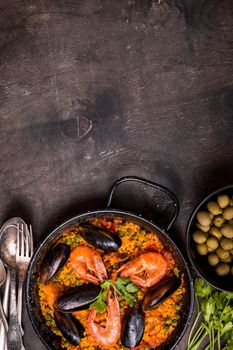 Paella background, space for text. Paella in black pan with saffron rice, peas, shrimps, mussels, squid, meat. Seafood paella, traditional spanish dish. Paella on rustic black wooden table. Top view