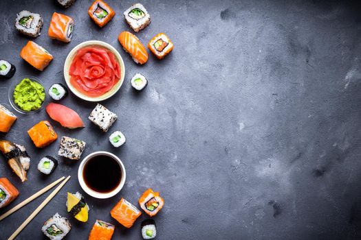 Japanese sushi on a rustic dark background. Sushi rolls, nigiri, maki, pickled ginger, wasabi, soy sauce. Sushi set on a table. Space for text. Top view. Sushi background. Asian or Japanese food frame