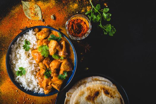 Indian Butter chicken with basmati rice in bowl, spices, naan bread. Black background. Space for text. Butter chicken, traditional Indian dish. Top view. Chicken tikka masala. Indian cuisine