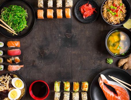 Sushi and japanese food on dark background. Sushi rolls, hiyashi wakame, miso soup, ramen, fried rice with vegetables, nigiri, salmon steak, soy sauce, сhopsticks. Asian/Japanese food frame. Overhead....