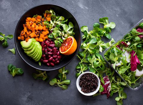 Quinoa salad in bowl with avocado, sweet potato, beans, herbs, orange on concrete rustic background. Quinoa superfood concept. Clean healthy detox eating. Vegan/vegetarian food. Making healthy salad