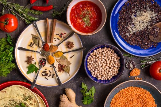 Assorted spices, herbs, chick-pea, lentil, basmati and wild rice mix, tomato chutney and pita on colorful plates. Top view. Spices and different food. Indian/ayurvedic food...