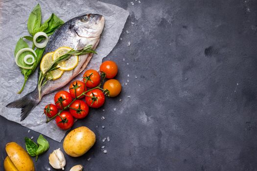 Raw fish with fresh ingredients ready to cook. Fish, lemon, herbs, potato, tomatoes. Ingredients for cooking on dark rustic background. Space for text. Diet and healthy food. Fish background. Top view