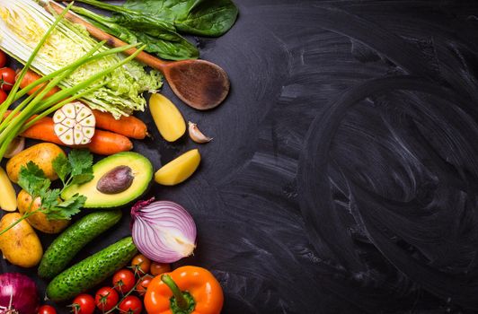 Vegetables, herbs, raw ingredients for cooking and wooden spoon on rustic black chalk board background. Healthy, clean eating concept. Vegan or gluten free diet. Space for text. Top view. Salad making