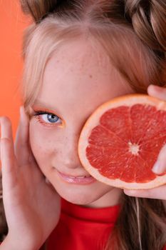 pretty tween girl in orange with a grapefruit isolated on orange background. tropical citrus fruit Grapefruit slices. orange stylish make up. teenager portrait.