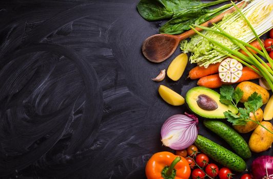 Vegetables, herbs, raw ingredients for cooking and wooden spoon on rustic black chalk board background. Healthy, clean eating concept. Vegan or gluten free diet. Space for text. Top view. Salad making