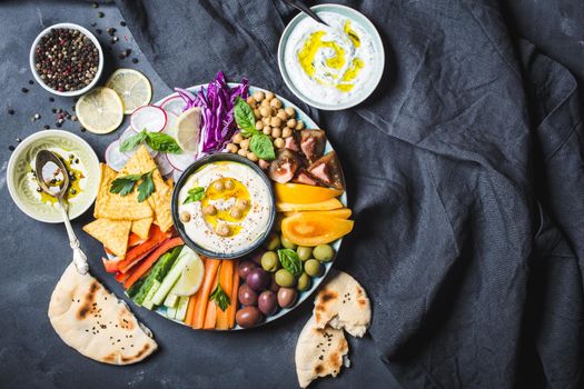 Meze platter with hummus, yoghurt dip, assorted snacks. Space for text. Hummus, vegetables sticks, chickpeas, olives, pita, chips. Plate, Middle Eastern/Mediterranean meze. Party/finger food. Top view